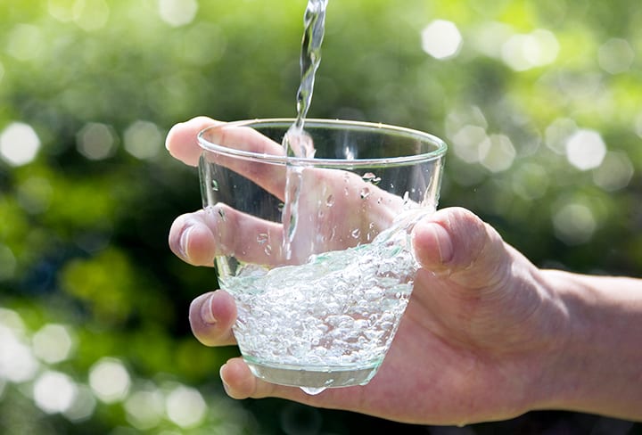 Fresh, clean water being poured into a clear glass held by a hand with a greenery background
